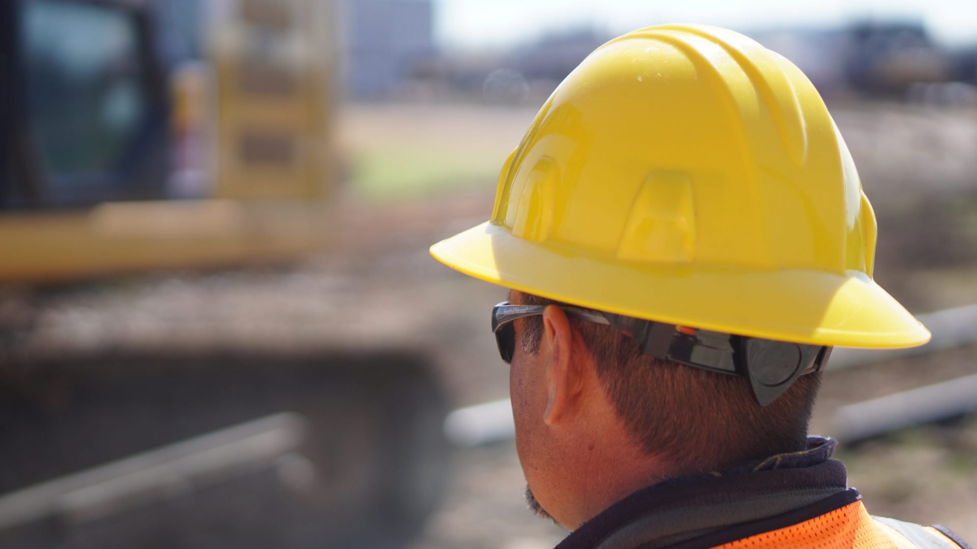 A railroad maintenance worker in a yellow hardhat observes a worksite.